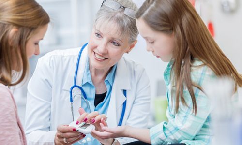 Senior pediatrician checks young girl's glucose level